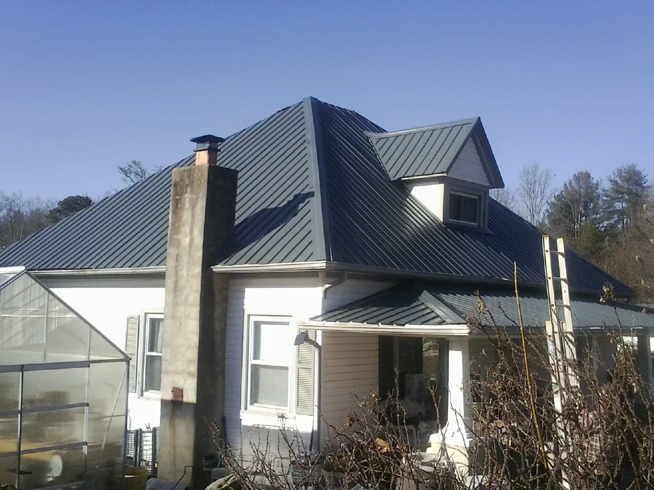 Dark blue standing seam metal roof on a white farmhouse with dormer — Slate & Tile Roof Repair by Roofing Brothers in Boulder