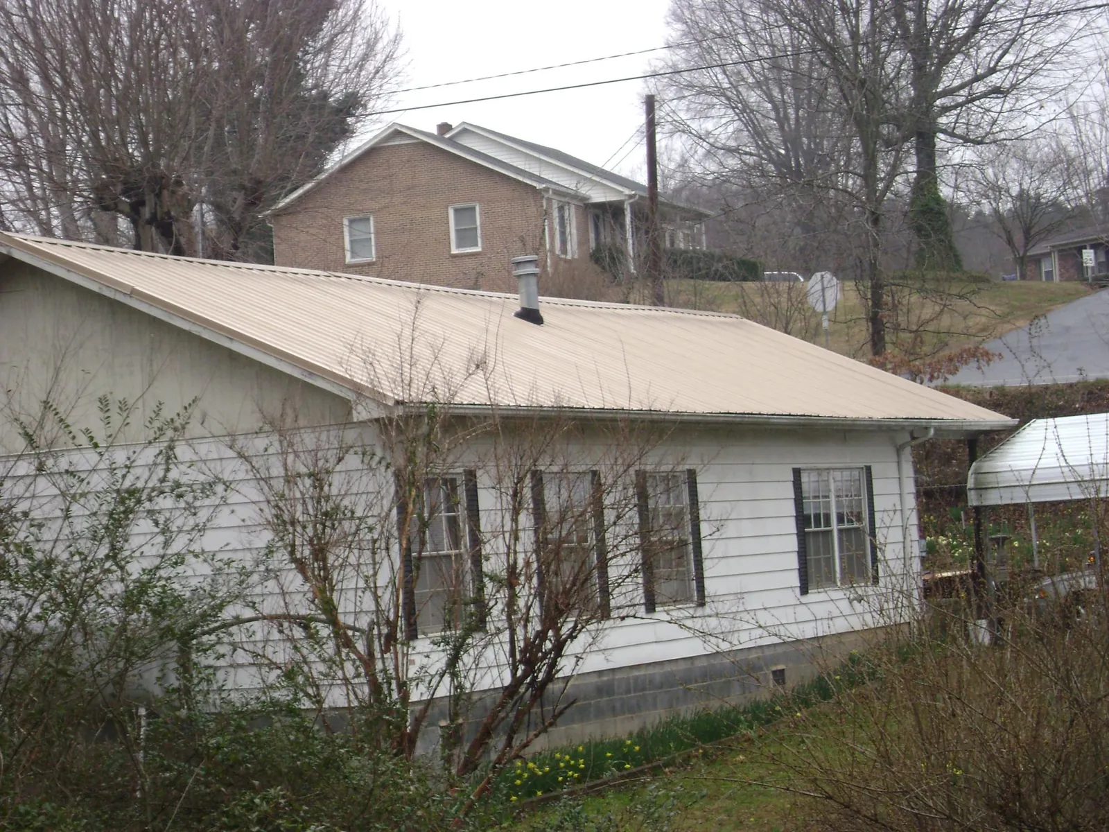Tan metal roof on a white sided house set into a hillside — Commercial Roofing by Roofing Brothers in Boulder